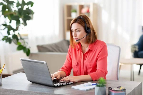 Kvinna med headset och bärbar dator arbetar hemma — Stockfoto