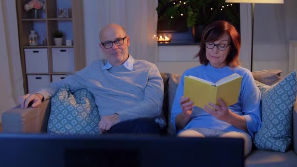 Пожилая пара смотрит телевизор и читает книги дома — стоковое видео