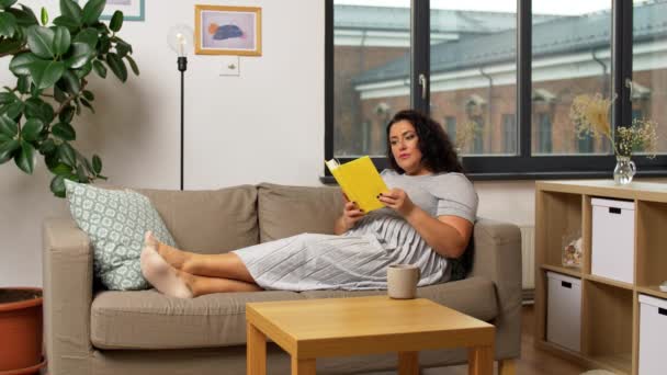 Heureuse jeune femme lecture livre sur canapé à la maison — Video