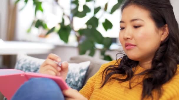 日記をつけたアジア系の女性が家でソファに座り — ストック動画