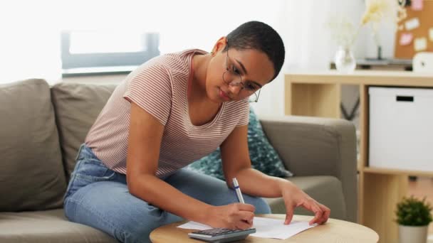 Femme africaine avec des papiers et calculatrice à la maison — Video