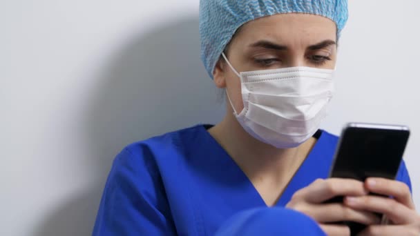 Smutny lekarz lub pielęgniarka w masce twarzy ze smartfonem — Wideo stockowe