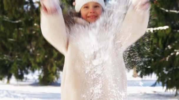 Χαρούμενο κοριτσάκι ρίχνει χιόνι στο χειμερινό πάρκο — Αρχείο Βίντεο