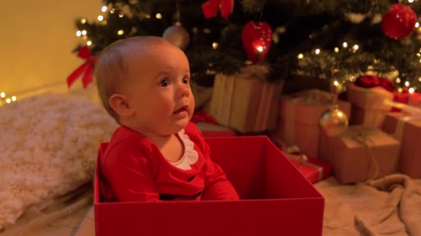 Menina sentada na caixa de presente sobre a árvore de natal — Vídeo de Stock