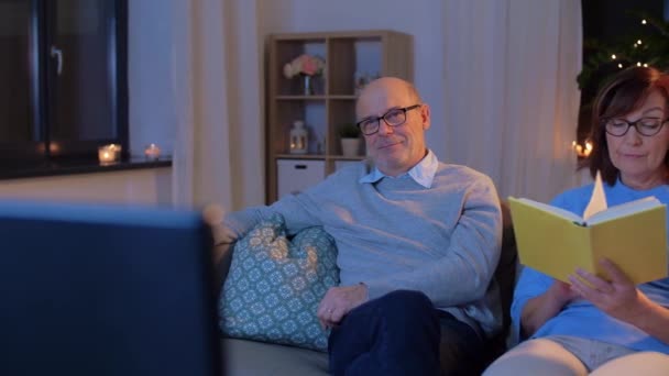 Seniorenpaar schaut Fernsehen und liest Buch zu Hause — Stockvideo