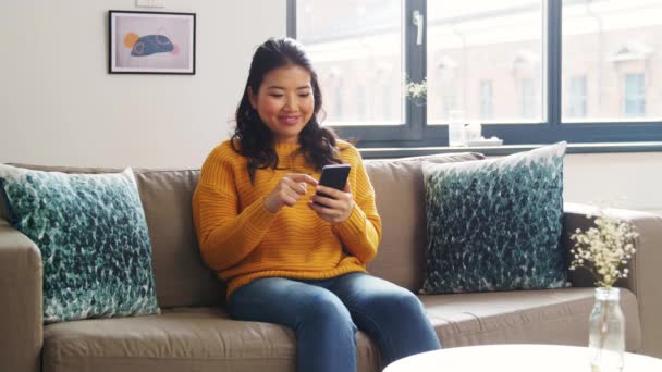 Lächelnde Asiatin mit Smartphone zu Hause — Stockvideo