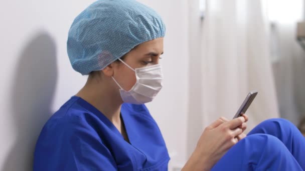 Грустный врач или медсестра в маске со смартфоном — стоковое видео