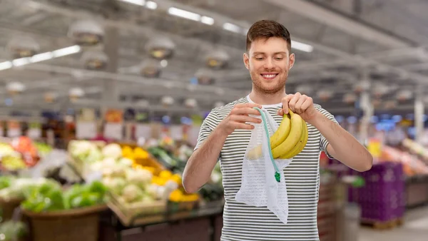 Uśmiechnięty mężczyzna wkładający banany do wielokrotnego użytku netto torby — Zdjęcie stockowe