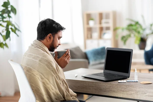 Sick young man in blanket drinking hot tea at home — Stock Photo, Image