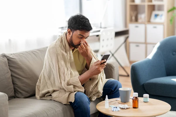 Άρρωστος νεαρός άνδρας σε κουβέρτα με smartphone στο σπίτι — Φωτογραφία Αρχείου