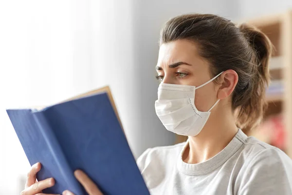 Zieke vrouw in medisch masker lezen boek thuis — Stockfoto