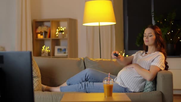 Terhes nő távirányítóval tv-t néz — Stock videók