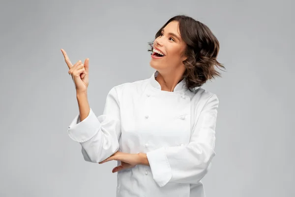 Glimlachende vrouwelijke chef-kok in toque wijzende vinger omhoog — Stockfoto