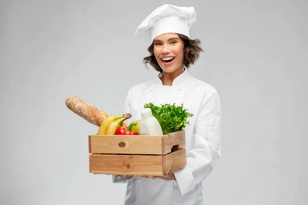 Glad leende kvinnlig kock med mat i trälåda — Stockfoto