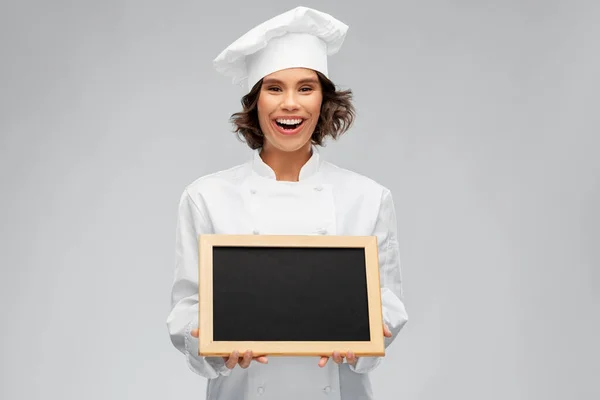 Usmívající se kuchařka drží černou tabuli — Stock fotografie