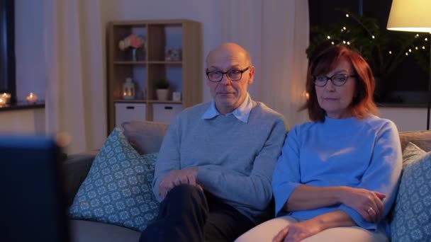 Счастливая пожилая пара смотрит телевизор дома вечером — стоковое видео