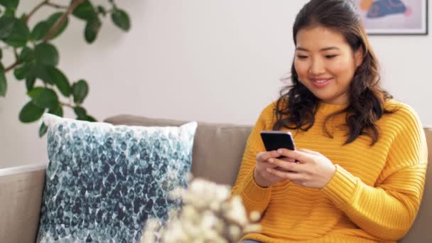 Lächelnde Asiatin mit Smartphone zu Hause — Stockvideo