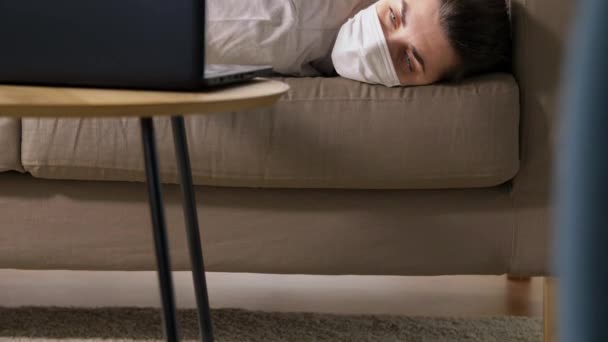 Больная скучающая женщина с ноутбуком лежит на диване дома — стоковое видео