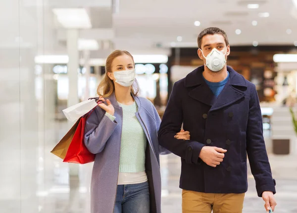 Casal em máscaras médicas com sacos de compras no shopping — Fotografia de Stock