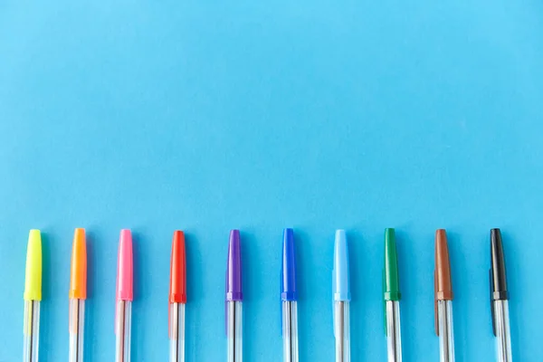 Ряд різнокольорових ручок на синьому фоні — стокове фото