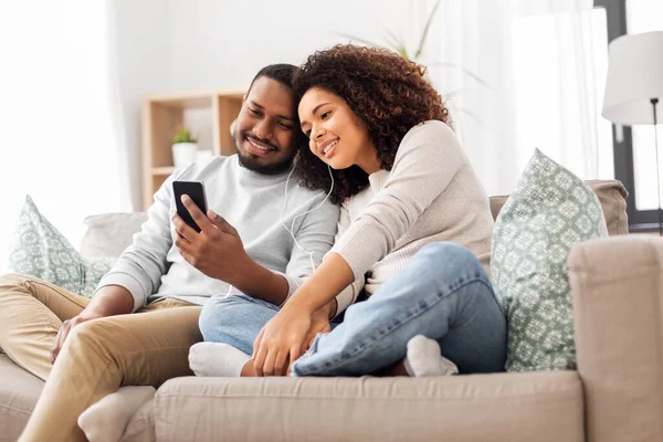 Szczęśliwa para ze smartfonem i słuchawkami w domu — Zdjęcie stockowe
