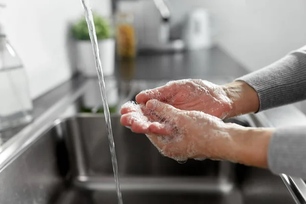 Женщина моет руки с жидким мылом на кухне — стоковое фото
