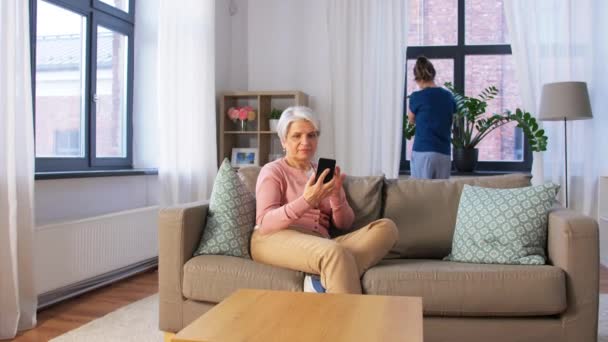 Vieille femme avec smartphone et femme de ménage à la maison — Video