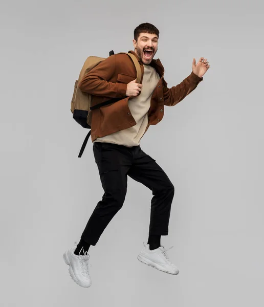 Leende ung man med ryggsäck hoppar i luften — Stockfoto