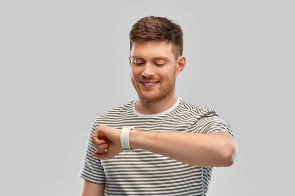 Uśmiechnięty młody człowiek patrząc na inteligentny zegarek — Zdjęcie stockowe