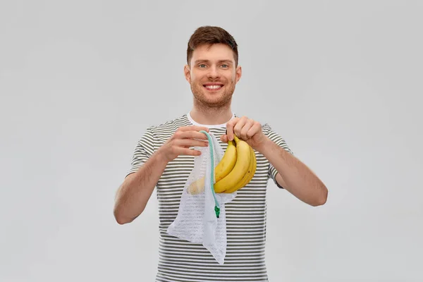 Усміхнений чоловік вставляє банани в багаторазовий чистий мішок — стокове фото