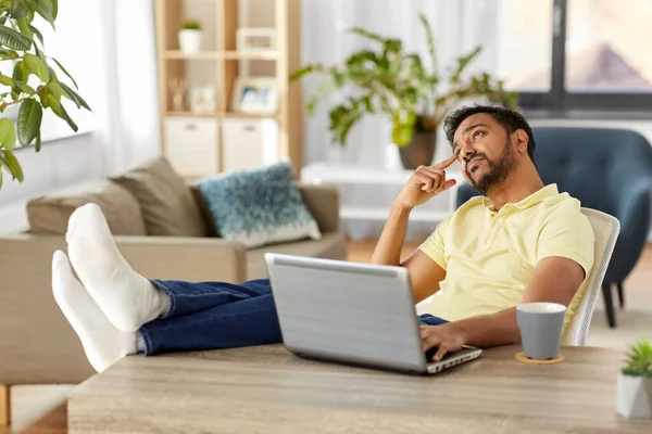 Hombre con portátil descansando los pies en la mesa en casa — Foto de Stock