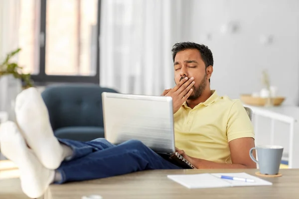 Vermoeide man met laptop en voeten op tafel thuis — Stockfoto