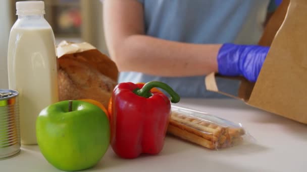 Vrouw in handschoenen het nemen van voedsel uit papieren zak thuis — Stockvideo