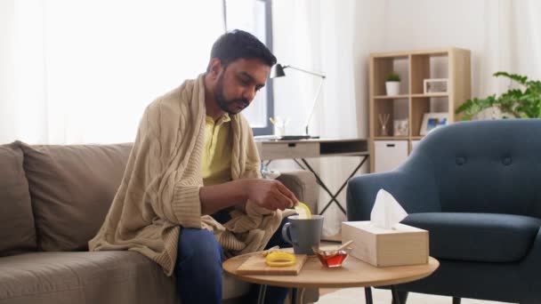 Хворий молодий чоловік у ковдрі п'є гарячий чай вдома — стокове відео