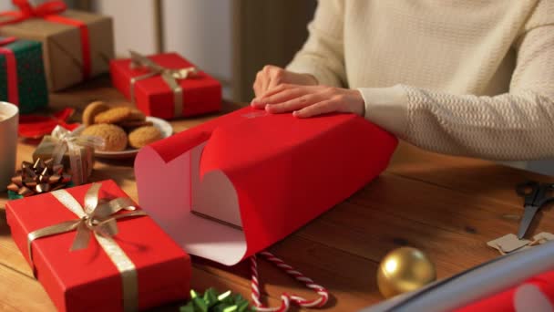 Женщина заворачивает рождественский подарок в бумагу дома — стоковое видео