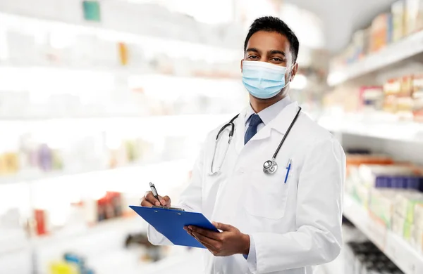 Médico indiano em máscara com prancheta na farmácia — Fotografia de Stock