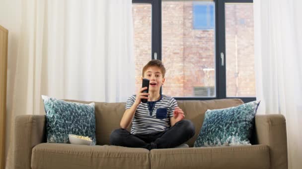 Мальчик с попкорном смотрит телевизор дома — стоковое видео