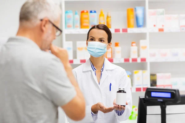 Apothecary in mask showing drug to man at pharmacy — Stock Photo, Image