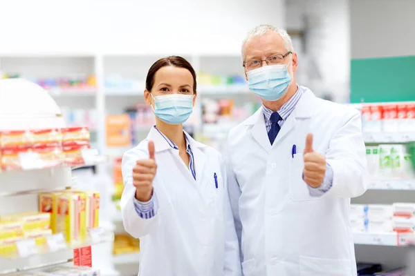 Boticários em máscaras mostram polegares na farmácia — Fotografia de Stock