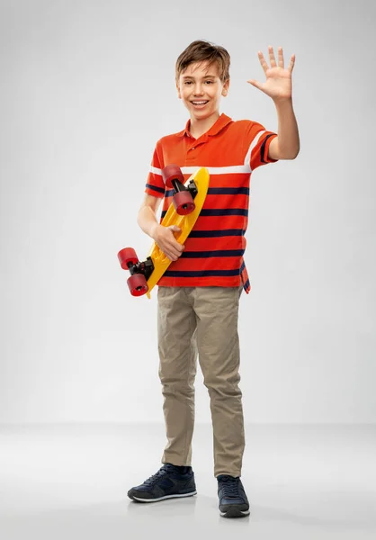 Улыбающийся мальчик с коротким скейтбордом машет рукой — стоковое фото