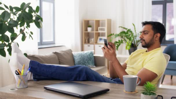 Hombre indio con smartphone descansando los pies en la mesa — Vídeos de Stock