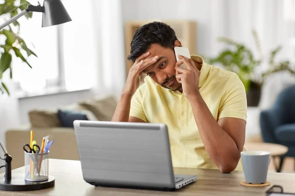 indian man with laptop calling on phone at home