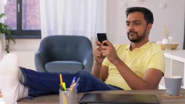 Indian man med smartphone vilar fötter på bordet — Stockvideo