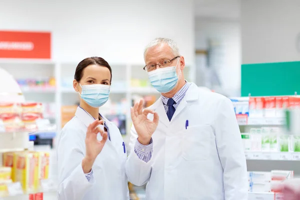 Boticários em máscaras na farmácia mostrando ok — Fotografia de Stock