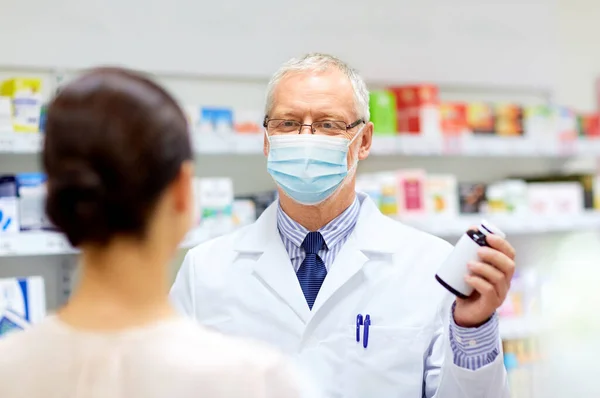 Apotheker met masker en medicijn en vrouw in de apotheek — Stockfoto