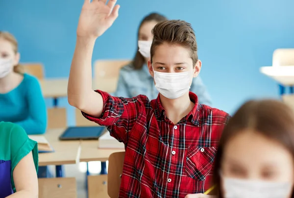Estudante menino em máscara com a mão levantada na escola — Fotografia de Stock