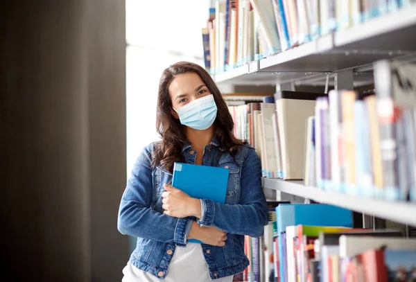 Estudante menina em máscara com livro na biblioteca — Fotografia de Stock