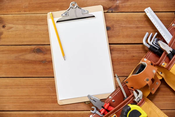 Presse-papiers, crayon et ceinture à outils sur des planches en bois — Photo