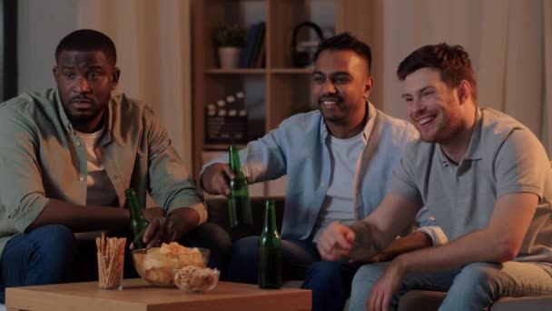 Друзья мужчины пьют пиво и смотрят телевизор дома — стоковое видео