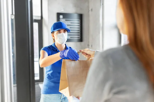 Entrega menina na máscara dando saco de papel ao cliente — Fotografia de Stock